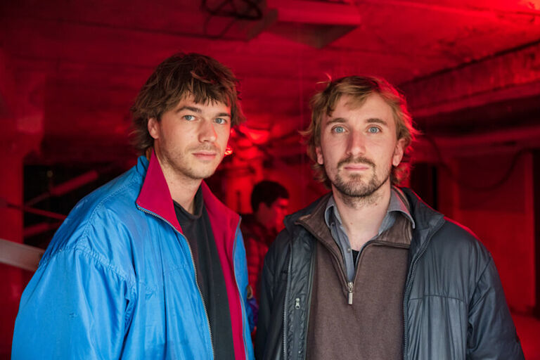 Foto der beiden Künstler in einem niedrigen Raum, er in rotes Licht getaucht ist