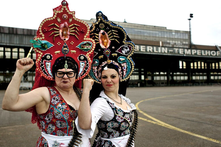 Die beiden Musikerinnen stehen in folkloritsichen Trachten und mit erhobener Faust vor dem Flughafengebäude in Tempelhof.