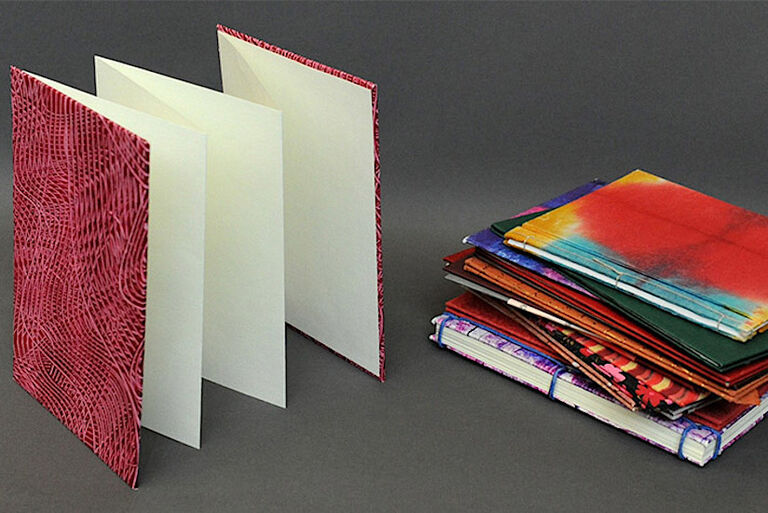 Auf einem Foto sind ein Leporello und ein Stapel farbenfroher kleiner Bücher und Hefte zu sehen.