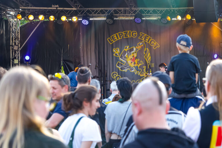 Vor einer Bühne mit einem Banner "Leipzig zeigt Courage" stehen viele Menschen