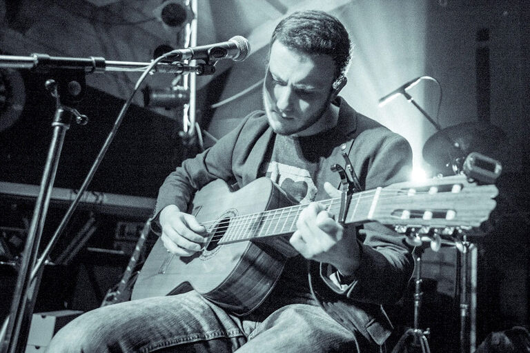 Schwarz-Weiß-Foto des Musikers, der mit konzentriertem Blick auf einer Bühne Gitarre spielt