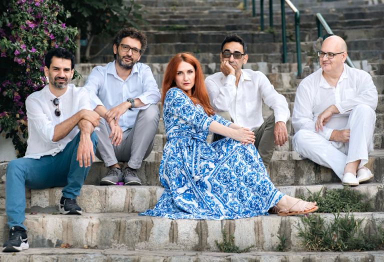 Die Sängerin und die Musiker des Ensembles sitzen auf einer alten Steintreppe.