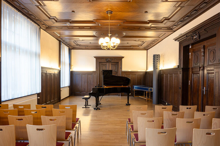 Blick in den Musiksalon der HMT mit Holzvertäfelungen an Decke und Wänden und einem Konzertflügel