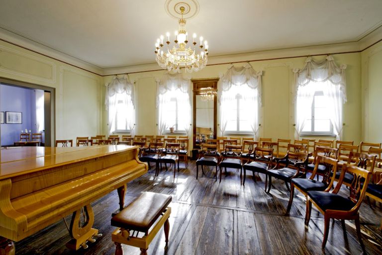 Im historischen Musiksalon mit Holzdielen und einem Kronleuchter an der Decke sind vier Stuhlreihen im Halbkreis um einen Konzertflügel aufgestellt.
