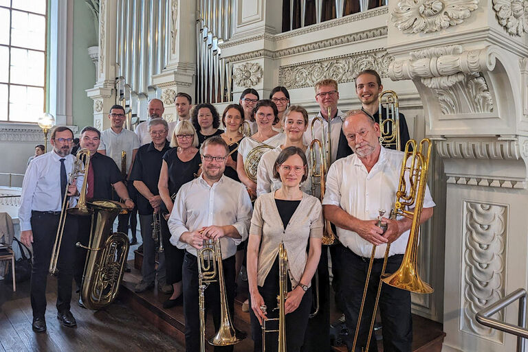 Die Musikerinnen und Musiker stehen mit ihren Instrumenten in einer Kirche vor einer eindrucksvoll verzierten Orgel