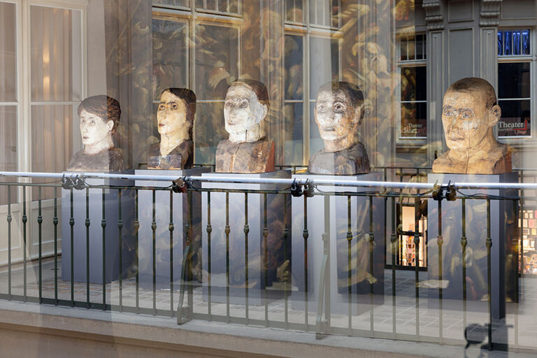 Fünf Skulpturen von Köpfen stehen nebeneinander in einem Schaufenster.