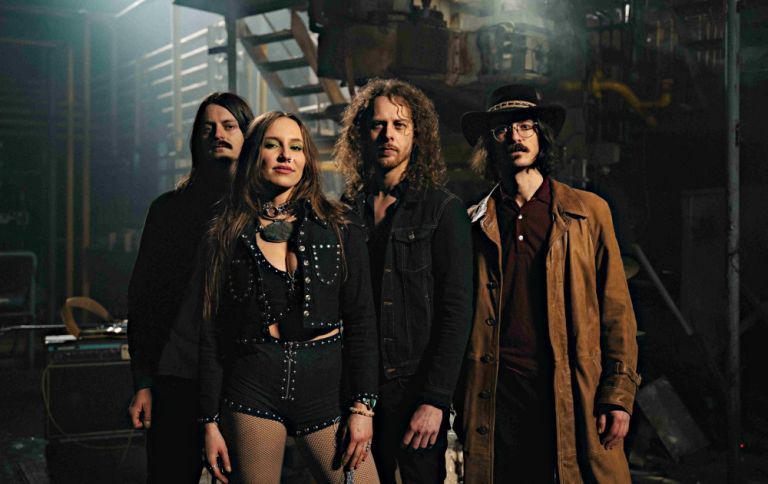 Gruppenfoto der Band in einem düsteren Raum mit einer Metalltreppe im Hintergrund