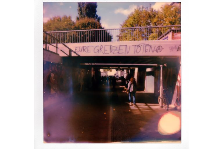 Vergilbtes Polaroid-Foto einer Unterführung an der steht: Eure Grenzen töten.