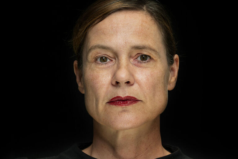 Ein Schauspielerin vor dunklem Hintergrung schaut ernst und streng in die Kamera