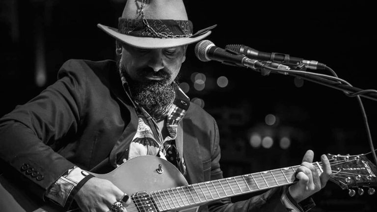 Schwarz-Weiß-Foto des Musikers mit Bart, Cowboyhut und Gitarre bei einem Auftritt