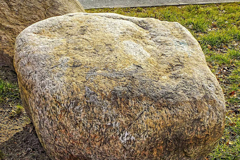Ein großer Naturstein liegt auf einer Wiese.