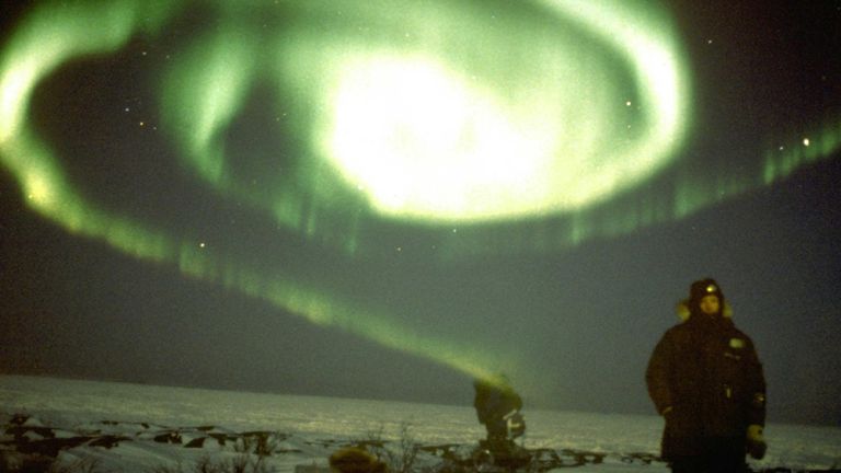 Leicht unscharfes Foto zweier Personen in der Arktis vor einem großartigen, spiralförmigen Nordlicht am Himmel