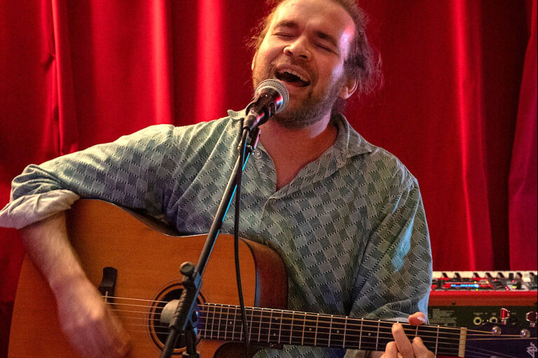 Der Sänger singt bei einem Konzert mit geschlossenen Augen zur Gitarre.