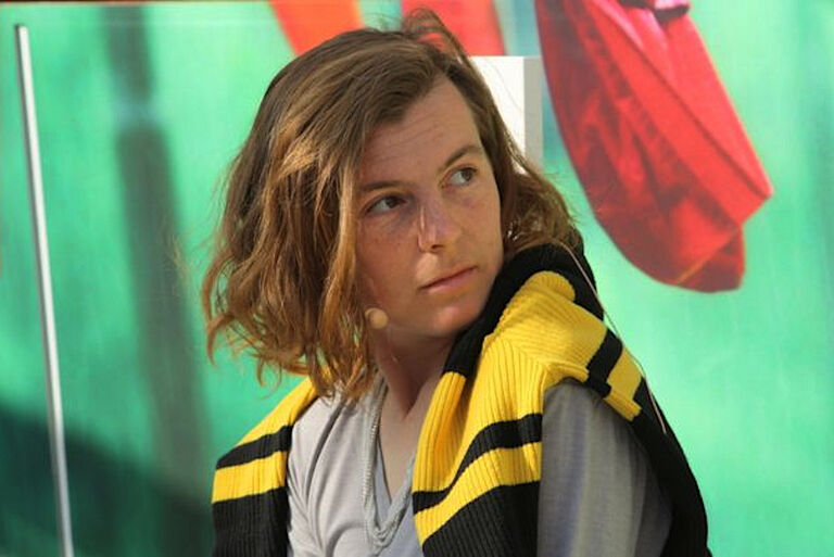 Die Autorin hat sich einen Pullover um die Schultern gelegt und schaut skeptisch zur Seite.