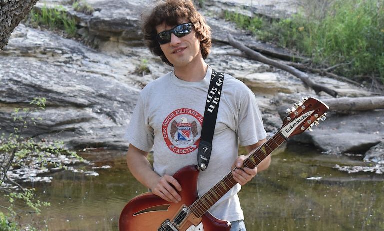 Foto des Musikers mit seiner Gitarre und Sonnenbrille vor einem kleinen Teich