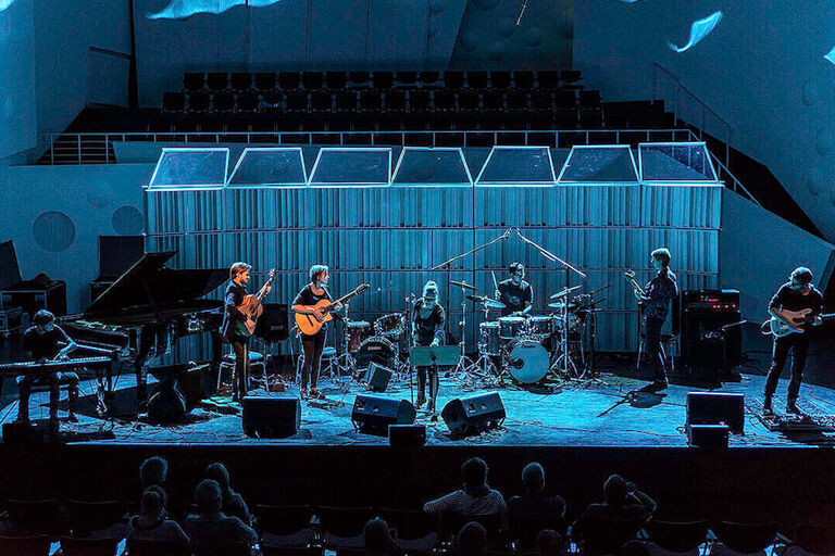 Auf einer großen Bühne spielen acht junge Musikerinnen und Musiker ein Konzert.