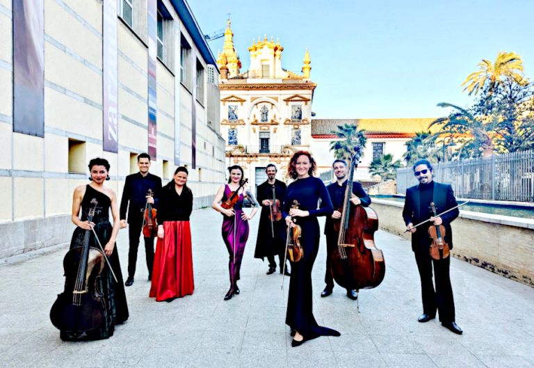 Gruppenfoto des Ensembles in Abendgardedrobe und mit seinen Instrumenten vor einem prachtvollem Kirchenbau