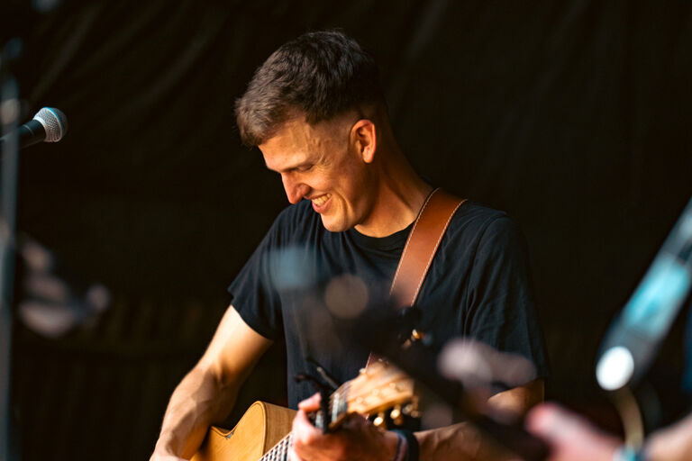 Konzertfoto von Johannes Scheurich mit seiner Gitarre in einem Moment, in dem er lächelnd nach untern schaut
