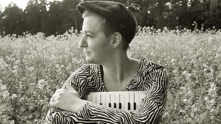 Die Musikerin sitzt mit ihrem Akkordeon in den Armen in einer blühenden Waldwiese.