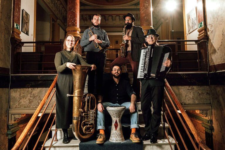 Gruppenfoto der Band mit ihren Instrumenten in einem herrschaftlichen Treppenhaus