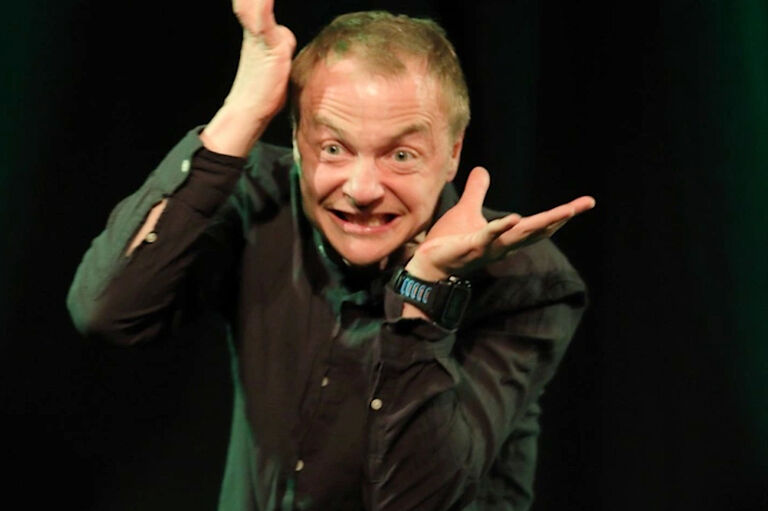 Ein Schauspieler hält seine hände neben dem kopf und zieht eine Grimasse.