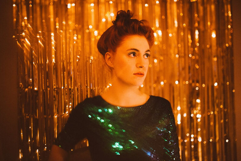 Portät von Lena Franke mit hochgesteckten Haaren in einem grünen Glitzerkleid vor einem goldenen Vorhang