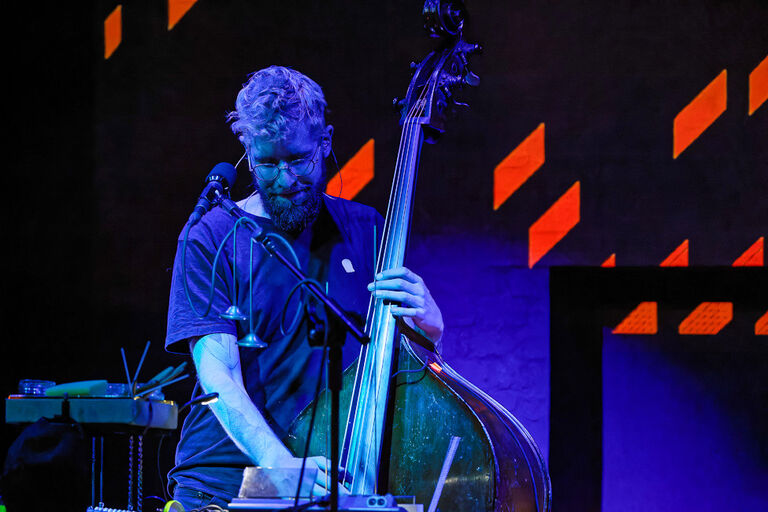 Der Musiker steht bei einem Konzert mit seinem Kontrabass auf der Bühne und wird von blauem Licht angestrahlt.