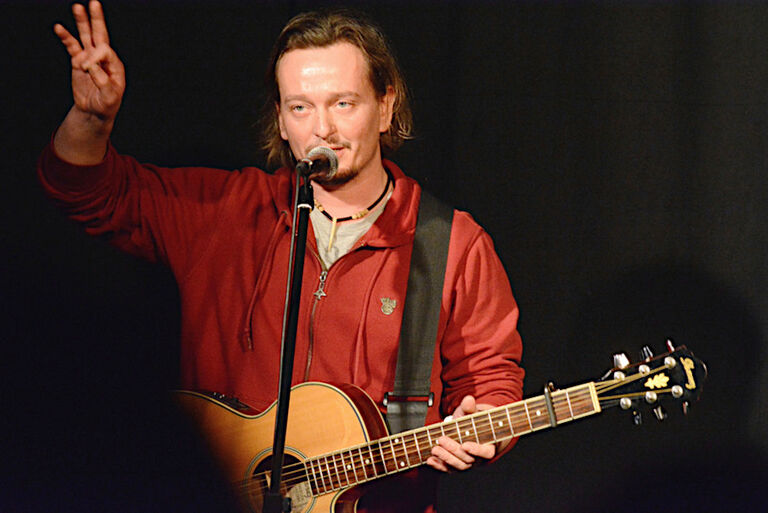 Foto des Sängers bei einem Auftritt mit Gitarre und hinter einem Mikrofon