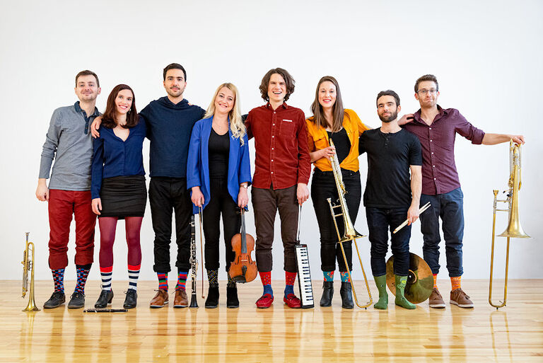 Gruppenfoto der fröhlich blickenden Musikerinnen und Musiker, die mit ihren Instrumenten nebeneinander stehen