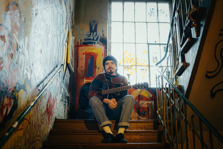 Der Musiker sitzt auf den Stufen eines mit Graffiti bedeckten Treppenhauses