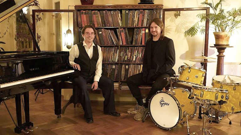 Die beiden Musiker sitzen in einem salonartigen Raum an ihren Instrumenten.