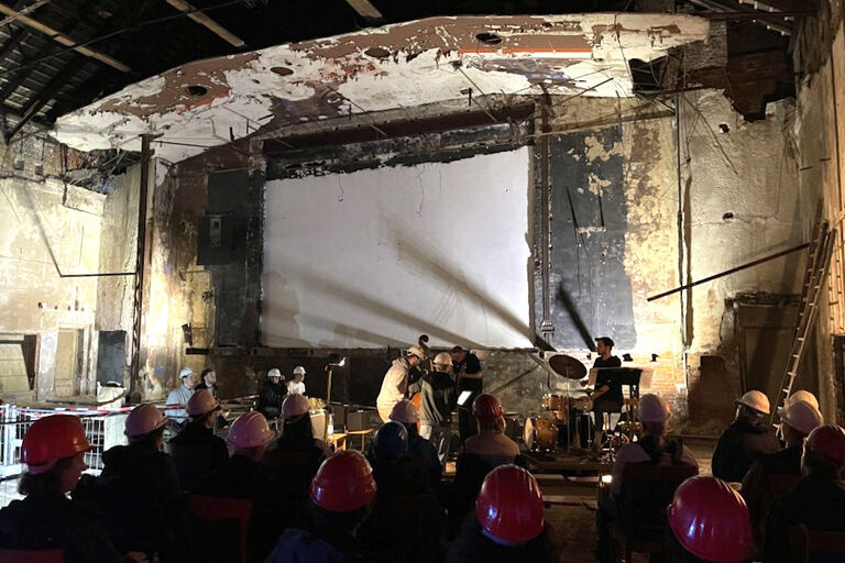 Konzert im notdürftig sanierten Kino der Jugend, bei dem die Band und das Publikum Bauhelme tragen