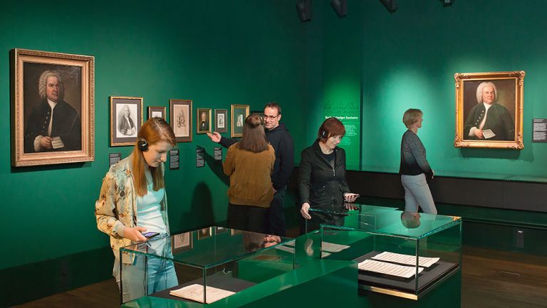 Blick in die Dauerausstellung in der an grnen Wänden Gemälde und Zeichnungen hängen und in Vitrinen originale Notenhandschriften von Bach zu sehen sind.