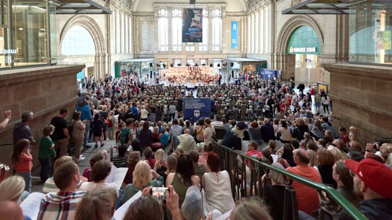 Blick in die große Osthalle des Leipziger Hauptbahnhofes, die gefllt ist mit Menschen die gemeinsam singen