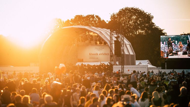 Die große Wiese im Rosental in Leipzig ist gefüllt mit Menschen die vor der Bühne und einer Videoleinwand im Sonnenuntergang dem Konzert folgen.