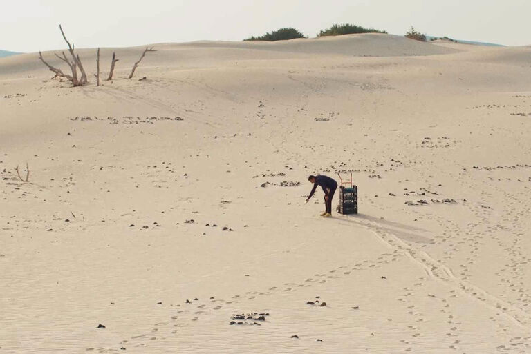 Eine Person schreibt auf einer weiten Sandfläche etwas auf den Boden
