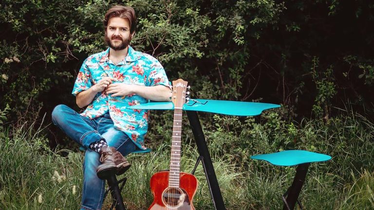 Richard Limbert sitzt auf einer grünen Wiese an einem Tich, an den seine Gitarre gelehnt ist