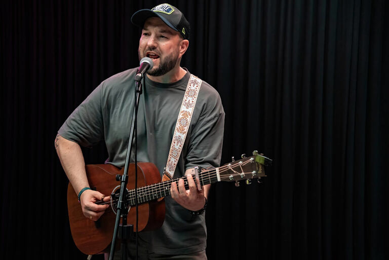 Der Musiker mit Gitarre und vor einem Mikrofon bei einem Auftritt