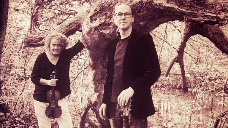 Foto des Duos im Wald an einem Tümpel mit einem großen umgestürzten Baum.