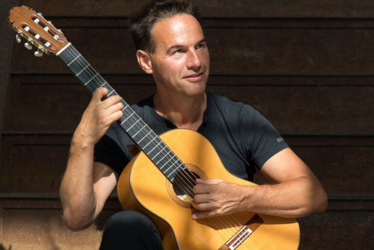 Uli Singer spielt lächelnd im Sonnenschein Gitarre