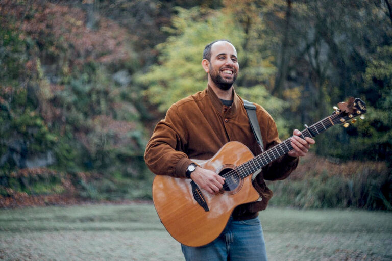 Der Musiker bei einem Auftritt mit Gitarre im Freien vor einem kleinen See.