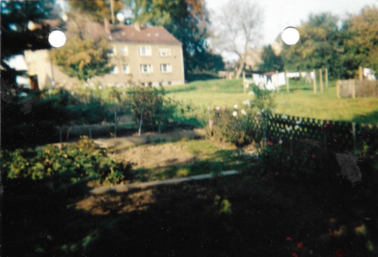 Unscharfes und leicht vergilbtes Foto eines alten Mehrfamilienhauses und einer Wiese, auf der Wäsche zum Trocknen hängt