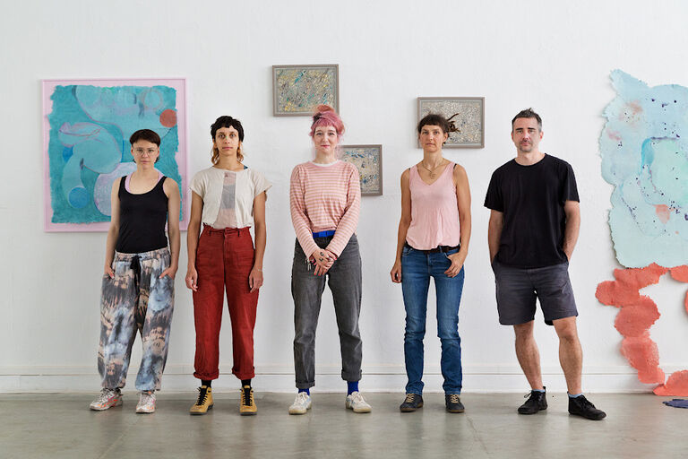 Die fünf Mitglieder des Lollektives stehen in einer Reihe vor einer weißen Wand mit ihren Kunstwerken.