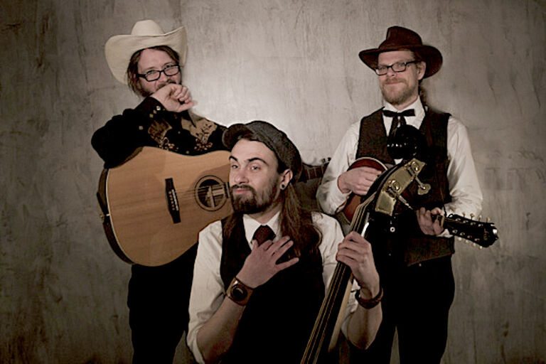 Gruppenfoto des verschmitzt blickenden Trios in Westernkleidung