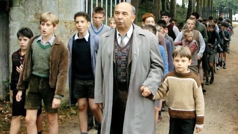 Filmszene in der Monsieur Mathieu mit seinen Jungen singend durch das Tor des Internats kommt.