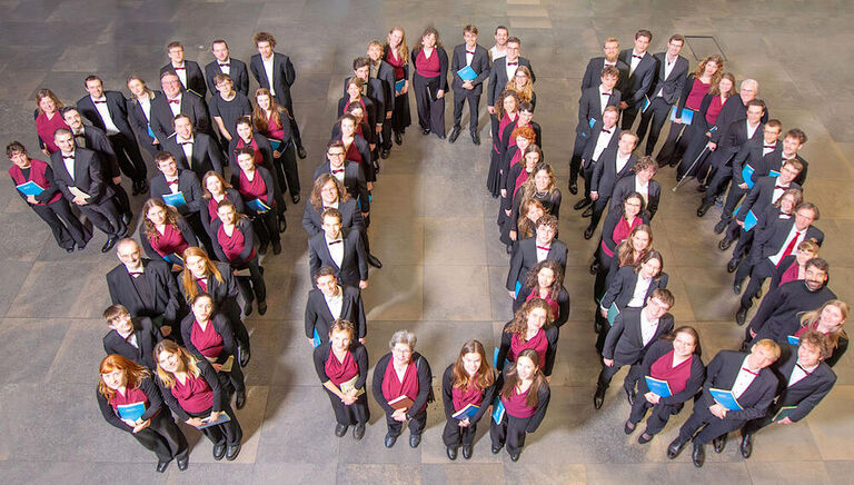 Gruppenfoto des Universitätschores, für das sich die Sängerinnen und Sänger in Form einer "100" aufgestellt haben