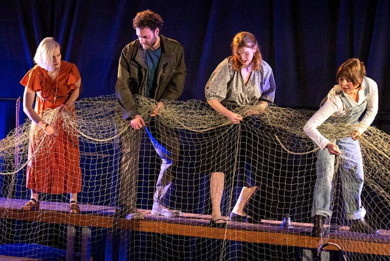 Drei Schauspielerinnen und ein Schauspieler holen gemeinsam auf der Bühne ein großes Fischernetz ein.
