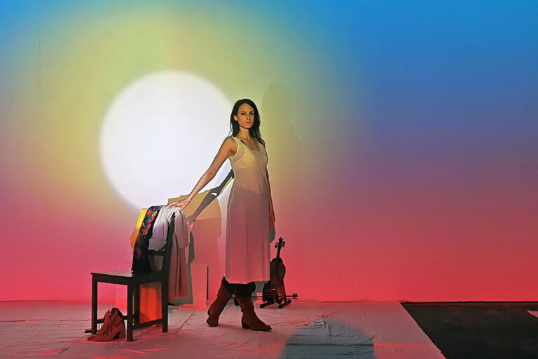 Die Musikerin steht im Unterrock neben einem Stuhl, über dessen Lehne eine ukrainische Tracht hängt.