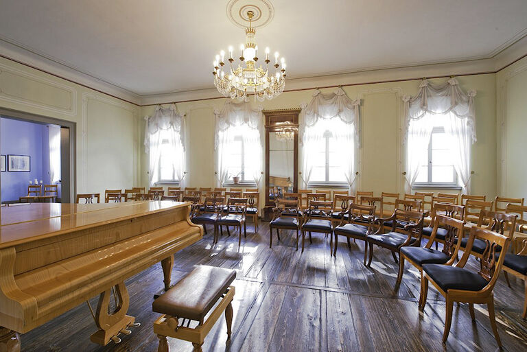Blick in den historischen Musiksalon mit einem Konzertflügel und mehreren Stuhlreihen