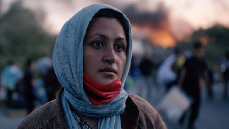 Foto von Nasim, im Hintergrund sieht man verschwommen viele Menschen mit ihren Habseligkeiten, Feuer und Rauch.